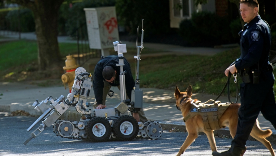 Law enforcement personnel monitor activity with a dog and operate a bomb disposal robot outside a post office which had been evacuated in Wilmington, Delaware, Oct. 25, 2018. Law enforcement personnel walks with a dog while another bends over a bomb disposal robot.