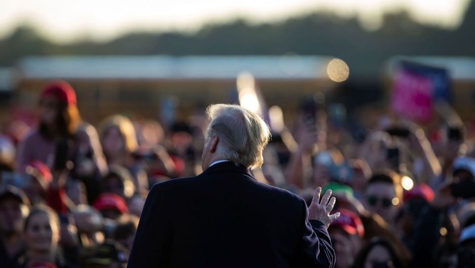 US President Donald Trump speaks to a crowd before a campaign rally at Southern Illinois Airport in Murphysboro, Illinois, Oct. 27, 2018. US President Donald Trump is photographed from behind with his right hand raised speaking to a crowd in the distance.