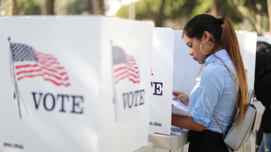 Desteny Martinez, 18, votes for the first time, in the US midterm elections in Norwalk, California, Oct. 24, 2018. A woman with a blue shirt and her hair pulled back is shown voting at a booth with an American flag and the word "vote" on the side.
