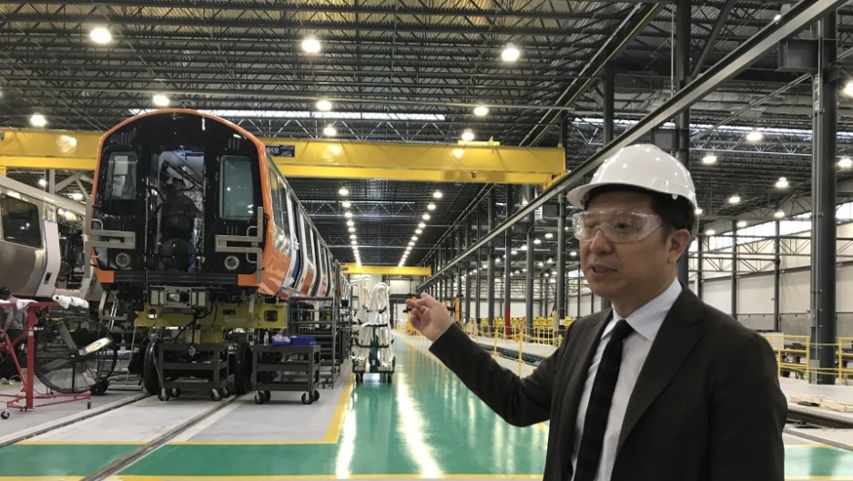a man with goggles and a protective helmet points to the factory behind him