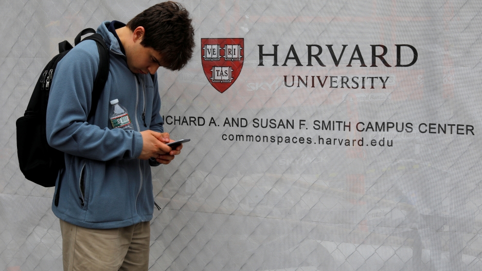 man in front of Harvard University sign looks at phone