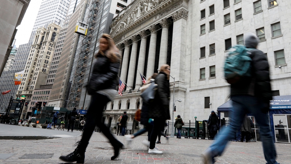 People walk on Wall Street in front of the New York Stock Exchange. People are shown in blurred motion walking in front of the New York Stock Exchange.