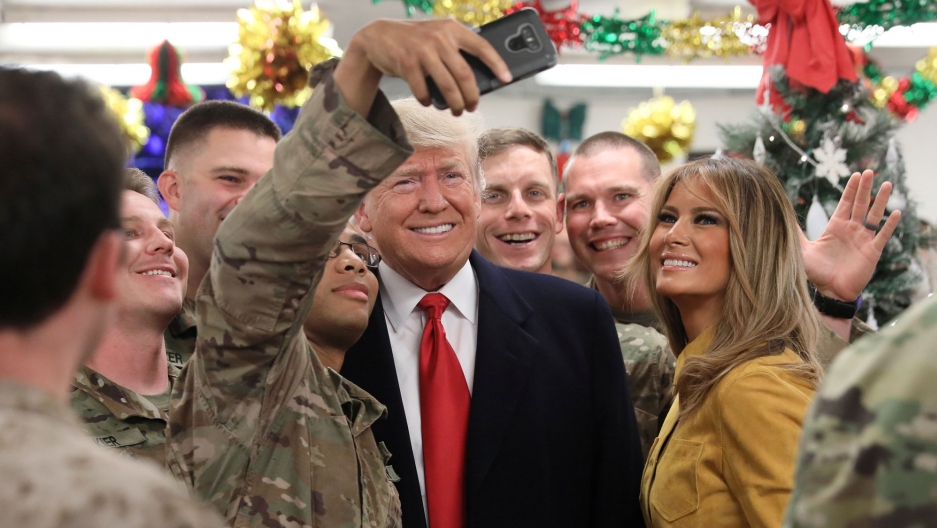 President Donald Trump and First Lady Melania Trump greet military personnel at Al Asad Air Base in Iraq, Dec 26, 2018. President Donald Trump and First Lady Melania Trump are shown surrounded by troops in camoflage while one soldier takes a selfie.