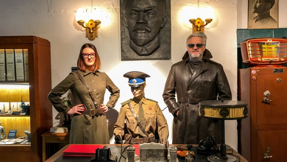Father-daughter curators Julius and Agne Urbaityte pose by the desk of a KGB duty officer wearing vintage military attire Father-daughter curators Julius Urbaitis and Agne Urbaityte pose behind a desk of a mannequin KGB duty officer wearing vintage military attire.