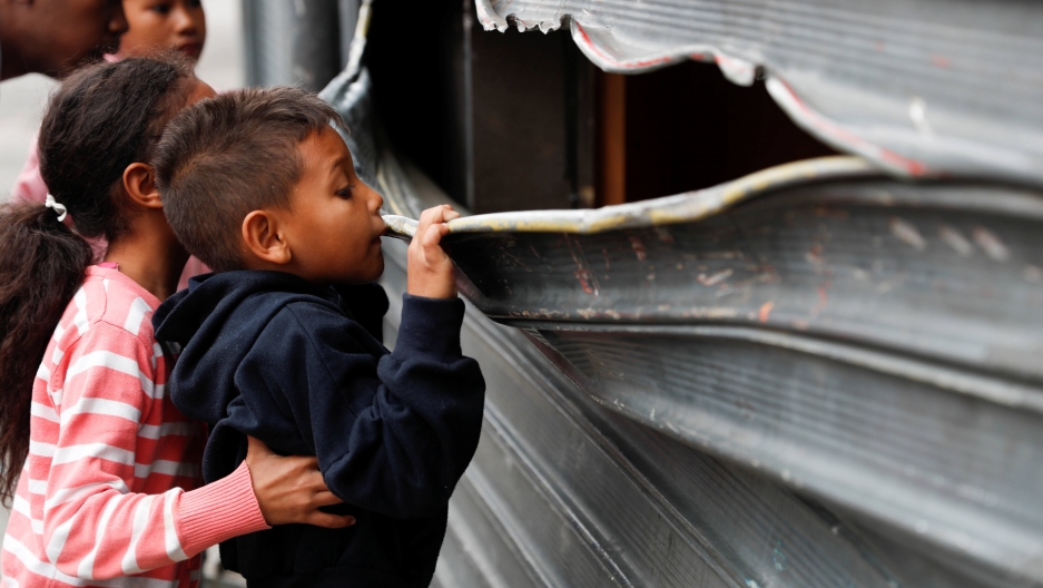 a small boy looks through the bent metal of a garage door