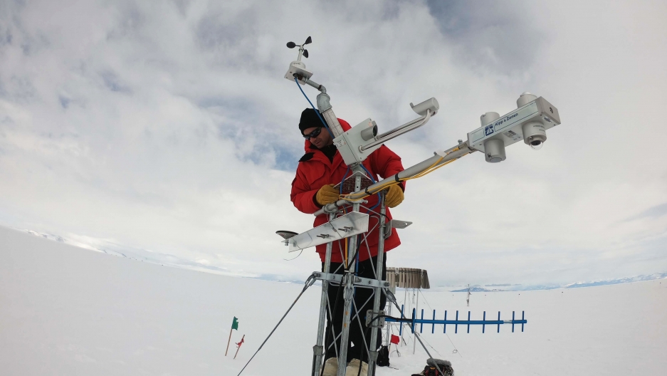 a man in a red coat stands on top of a large research instrument