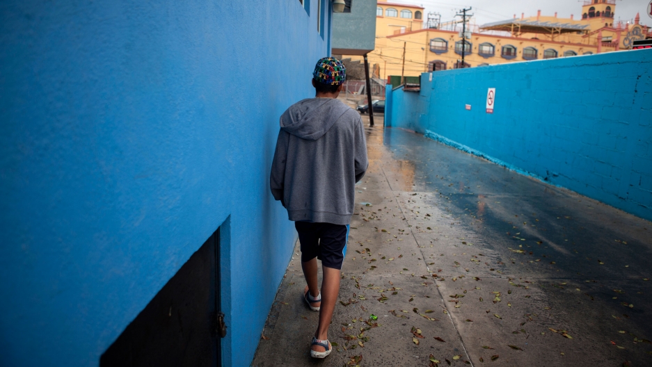 A teenage walks down a driveway next to a bright blue building