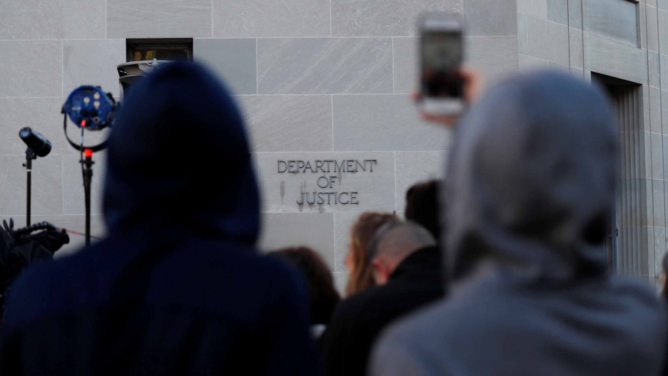 A crowd of people stand outside a the Department of Justice building 