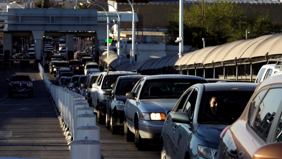 Drivers wait in line to cross to El Paso, Texas, on the international border crossing bridge. Cars are lined up across the entire distance of the photograph — in line to cross to El Paso, Texas.