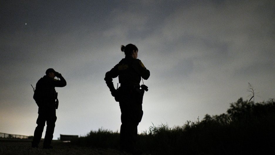 US Border Patrol agents search for undocumented migrants near Palmview, Texas, April 6, 2019. Two Border Patrol agents are shown in silhouette looking off in a darkened field.