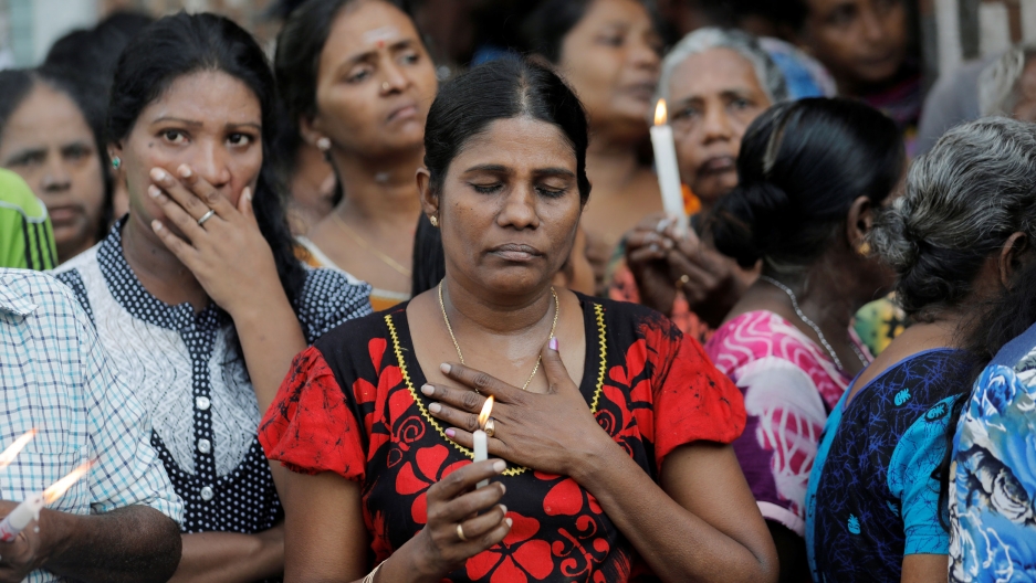 People react as silence is observed as a tribute to victims two days after a string of suicide bomb attacks in Sri Lanka. A woman is show standing with her eyes closed and a holding a candle.