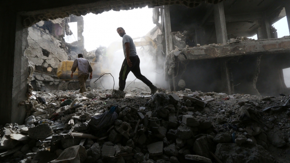 Workers search for bodies still trapped under mounds of debris in Raqqa, Syria, 2018. A man is shown walking through the rubble of a destroyed building in Syria.
