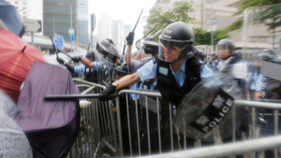Protesters clash with riot police during a demonstration near the Legislative Council in Hong Kong, China, June 12, 2019. A police officer is shown with a helmet and clear face mask down, striking a person with an umbrella with his batton.