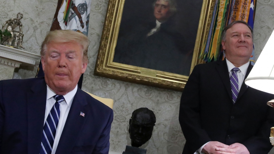 US President Donald Trump speaks as Secretary of State Mike Pompeo stands by in the Oval Office, June 20, 2019. US President Donald Trump is shown sitting and looking to his left with Mike Pompeo standing behind him to his left.