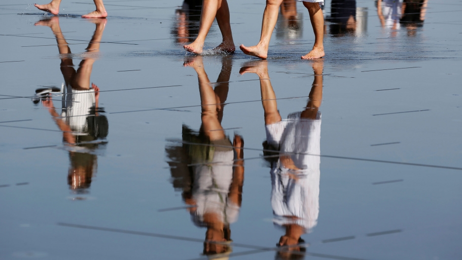 People cool off on the Miroir d'Eau, during sweltering June temperatures, in Bordeaux, France, June 26, 2019. The reflection of several women are shown in water with just the bottom part of their legs shown at the top of the photograph.