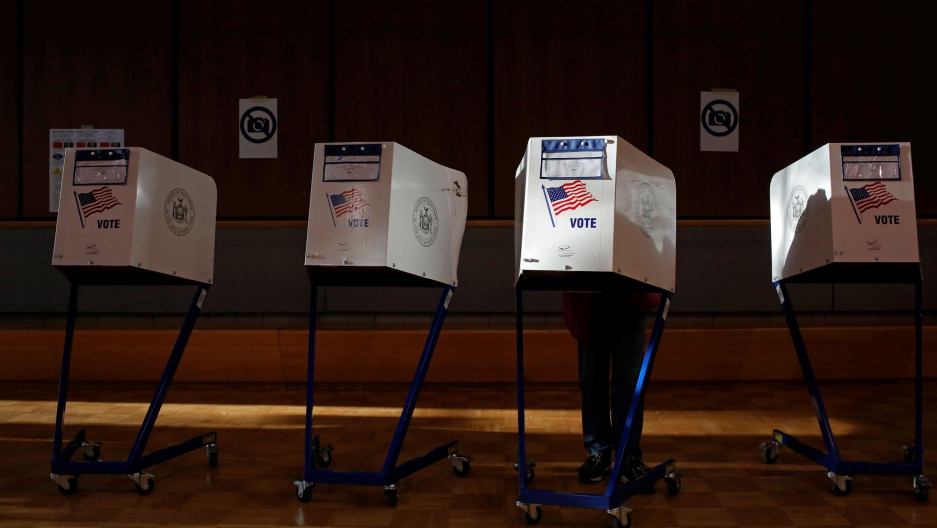 A woman fills out a ballot for the US presidential election at the James Weldon Johnson Community Center in the East Harlem neighborhood of Manhattan, New York City, November 8, 2016. Four stand-alone voting booths are shown with US flags and the word 'vote' printed on the,