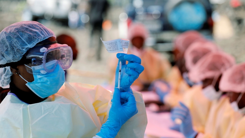 A health worker fills a syringe with Ebola vaccine before injecting it to a patient, in Goma, Democratic Republic of Congo, Aug. 5, 2019. A medical worker is shown wearing a mask, goggles and hair covering while holding a syringe.