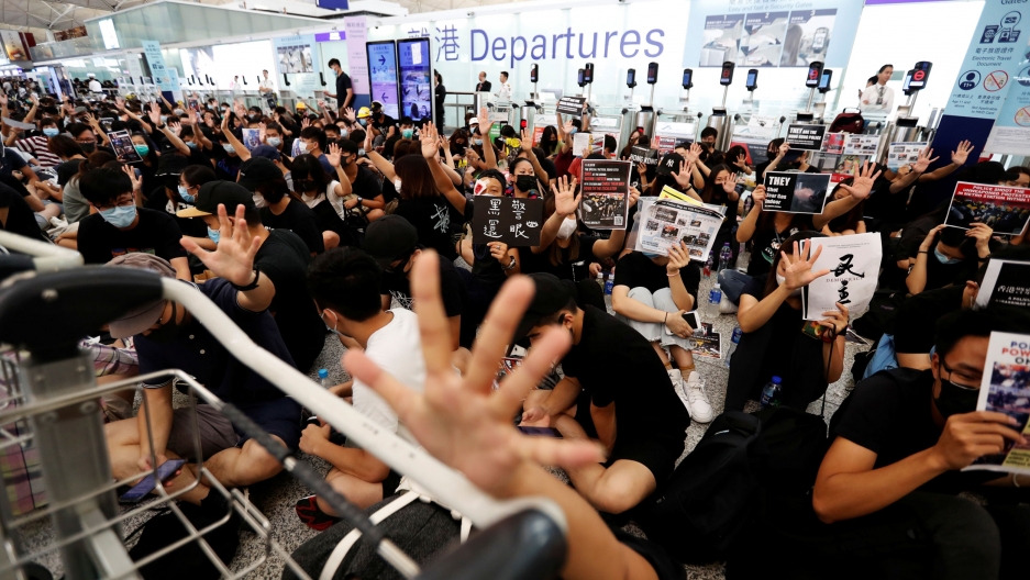 Anti-government protesters react after the announcement that all airport operations are suspended due to a demonstration at Hong Kong Airport, Aug. 13, 2019. A crowd of demonstrators are shown with their hand in the air and hiding their face in Hong Kong Airport.