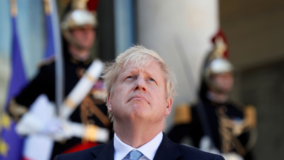 British Prime Minister Boris Johnson is shown before a meeting on Brexit at the Élysée Palace in Paris, France, Aug. 22, 2019. British Prime Minister Boris Johnson is shown looking up and wearing a suit and blue tie with Élysée Palace guards in soft focus in the background.
