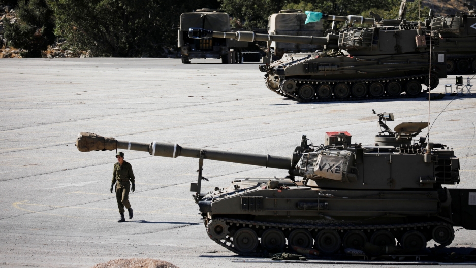 An Israeli soldier walks next to a mobile artillery unit near the Israeli side of the border with Syria in the Golan Heights, Aug. 26, 2019. A soldier is shown walking next to a large tank with another tank in the background.