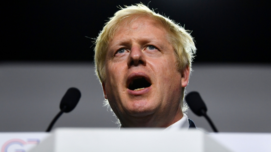 Britain's Prime Minister Boris Johnson speaks during a news conference, Aug. 26, 2019. Britain's Prime Minister Boris Johnson is shown standing behind two small microphones with his mouth open speaking.