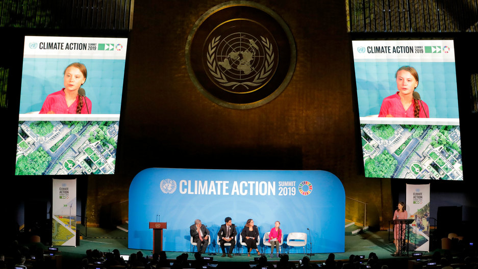 Swedish climate activist Greta Thunberg, 16, speaks at the 2019 United Nations Climate Action Summit at the UN headquarters in New York City on Sept. 23, 2019. Greta Thunberg is shown sitting on a stage wearing a pink shirt with a video projection of her above.