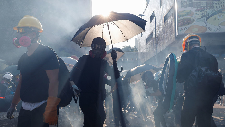Anti-government protesters react in a cloud of tear gas during a demonstration on China's National Day in Hong Kong, China, Oct. 1, 2019. Several people are shown shrowded in smoke with one person holding a dark umbrella up to refract the sunlight.