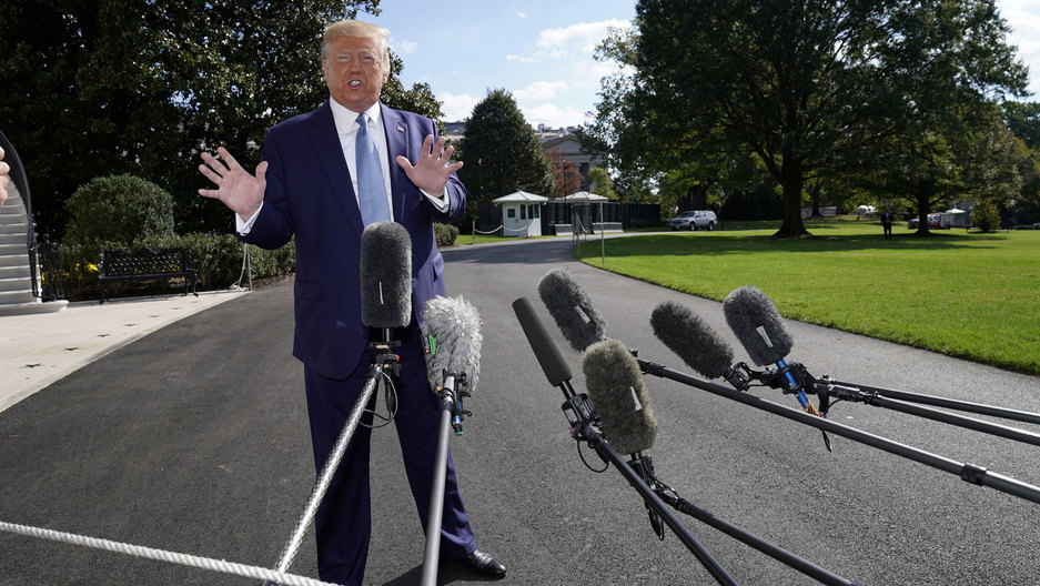 US President Donald Trump talks to reporters as he heads to the Marine One helicopter to fly from the South Lawn in Washington, DC, Oct. 4, 2019. US President Donald Trump is shown standing with his hands out and wearing a blue suit with microphones in the nearground.