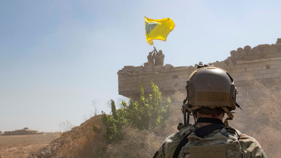 A US soldier oversees members of the Syrian Democratic Forces at an outpost as part of the security mechanism zone agreement, in Syria. A US soldier is seen in the nearground wearing full battle fatigues and looking out on two members of the Syrian Democratic Forces.