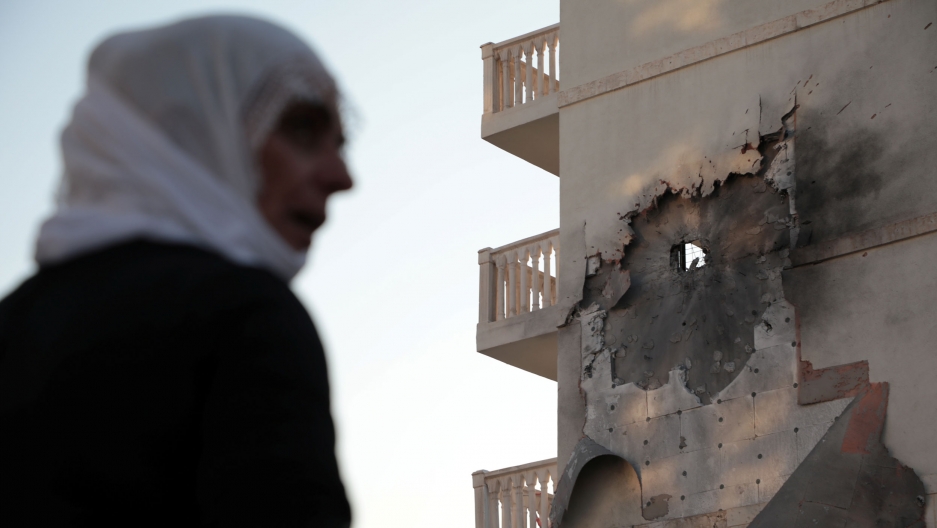 A woman stands in front of an apartment building damaged by a rocket fired from Syria, in Nusaybin, Turkey, Oct. 10, 2019. A woman is shown in soft focus in the nearground with an apartment building in the background that has bombed.