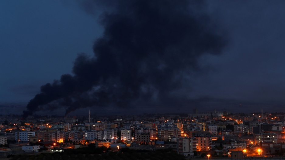 Smoke rises over the Syrian town of Ras al Ain, as seen from the Turkish border town of Ceylanpinar, Oct. 16, 2019. Black smoke is show rises from the Syrian town of Ras al Ain as night falls and streetlights glow.