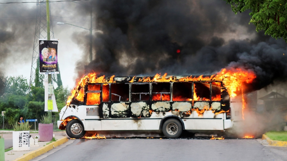 A burning bus, set alight by cartel gunmen to block a road, is pictured during clashes with security forces following the detention of Joaquin "El Chapo" Guzman's son, in Culiacan, Mexico, Oct. 17, 2019. A white bus is shown ablaze and blocking a road with black smoke coming from it.