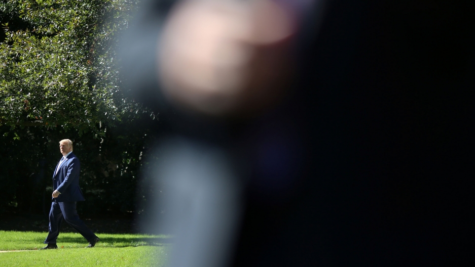 US President Donald Trump leaves the White House as he departs for travel to Pennsylvania, Oct. 23, 2019. US President Donald Trump is shown in the distance wearing a suit and walking on a sidewalk.