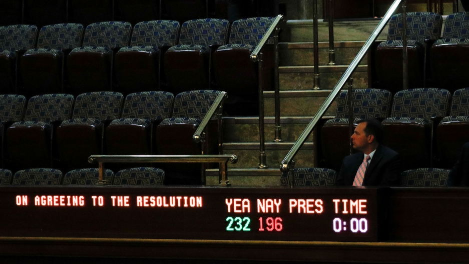 A man sits in the visitors gallery above the floor of the US House of Representatives as a display board shows the final vote tallies on a resolution that outlines the next steps in the impeachment inquiry of President Donald Trump. A man is shown sitting in the balcony of the US House with a vote tallying electric sign in front of him.