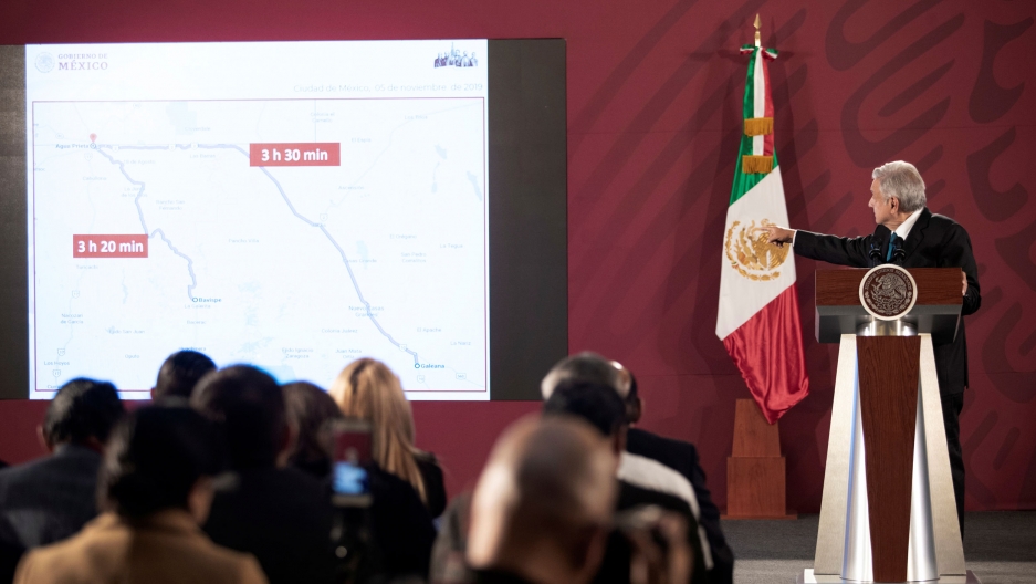 Mexico's President Andrés Manuel López Obrador shows a map of the area where several members of a family were killed near the US border, Nov. 5, 2019. Mexico's President Andrés Manuel López Obrador is shown standing at a podium pointing toward a projection of a map with the Mexican flag behind him.