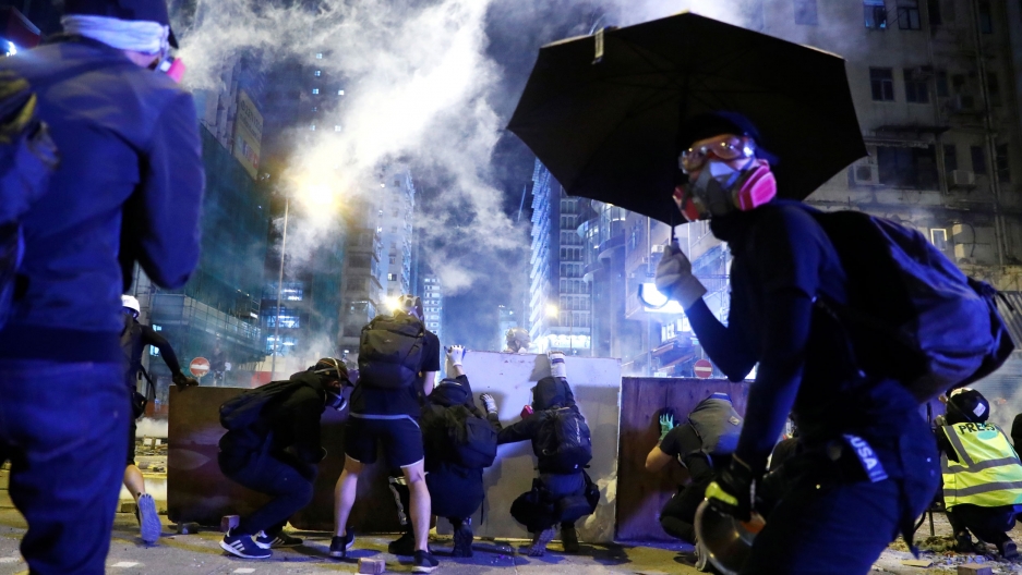 Protesters take cover behind boards during a protest in the Mong Kok area in Hong Kong, Nov. 11, 2019. Several protesters are seen crouching behind boards and wearing all black with another protester wearing a gas mask and holding an umbrella.