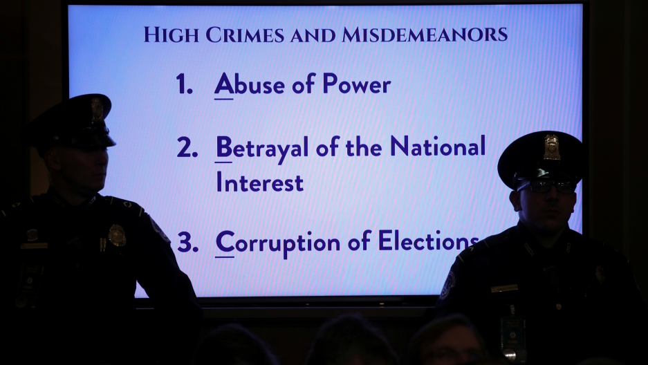 US Capitol police officers watch from in front of a video monitor displaying definitions of "High Crimes and Misdemeanors" as the House Judiciary Committee holds their first hearing on the impeachment inquiry into US President Donald Trump, Dec. 4, 2019. US Capitol police officers are shown in shadow standing in front of a brightly lit TV monitor displaying several sentences of text related to US President Donald Trump's alleged impeachable offenses.