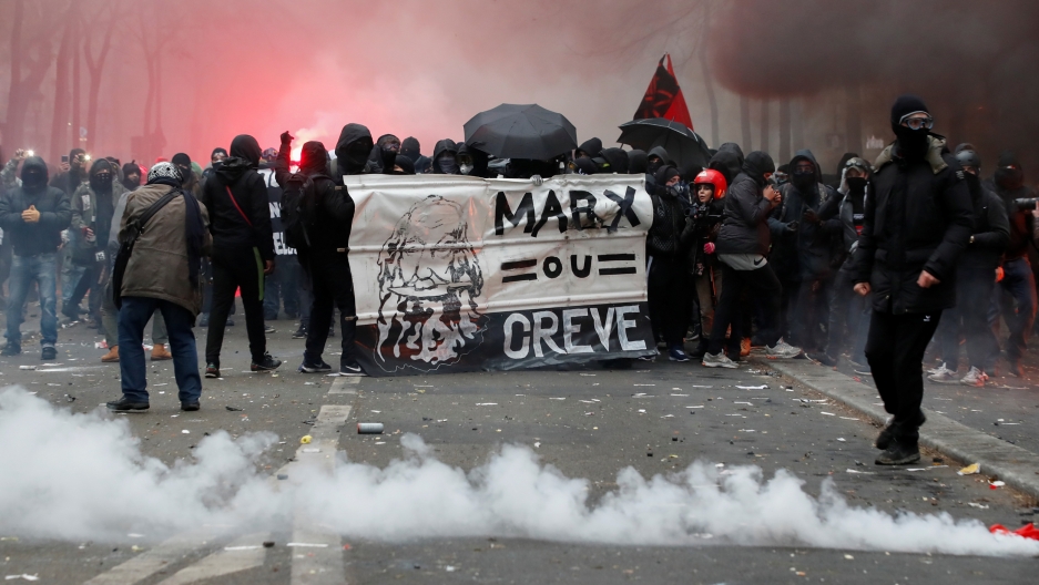 Protesters attend a demonstration against French government's pensions reform plans, as part of a day of national strike and protests, in Paris, France, Dec. 5, 2019. A large group of protesters are shown in a smoke-filled street wearing dark clothes and face masks and carrying a banner.