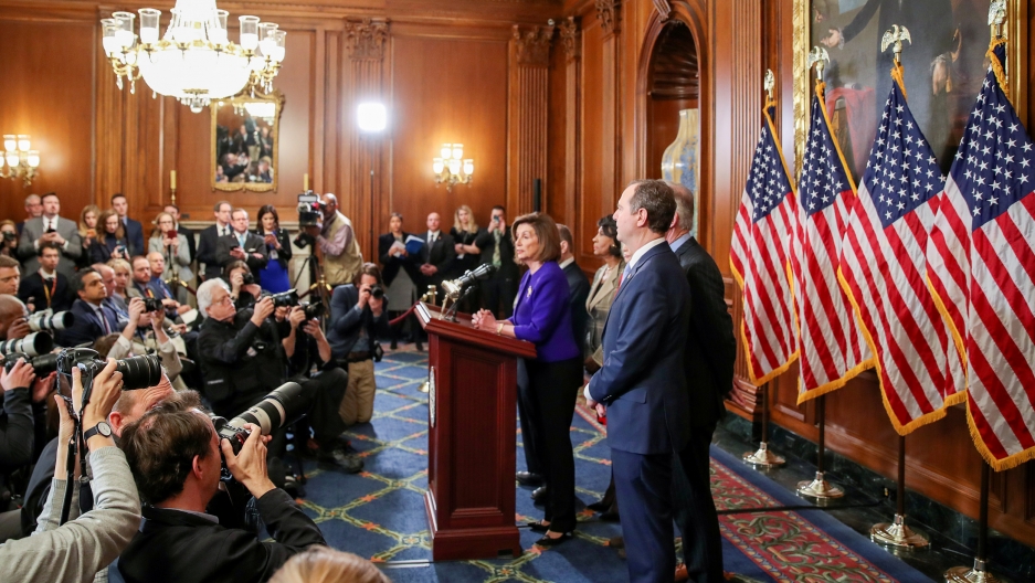 House Speaker Nancy Pelosi stands with other members of the House announcing articles of impeachment against President Donald Trump in Washington DC, Dec. 10, 2019. House Speaker Nancy Pelosi is shown standing at a wooden podium with microphones and several lawmakers standing behind her.