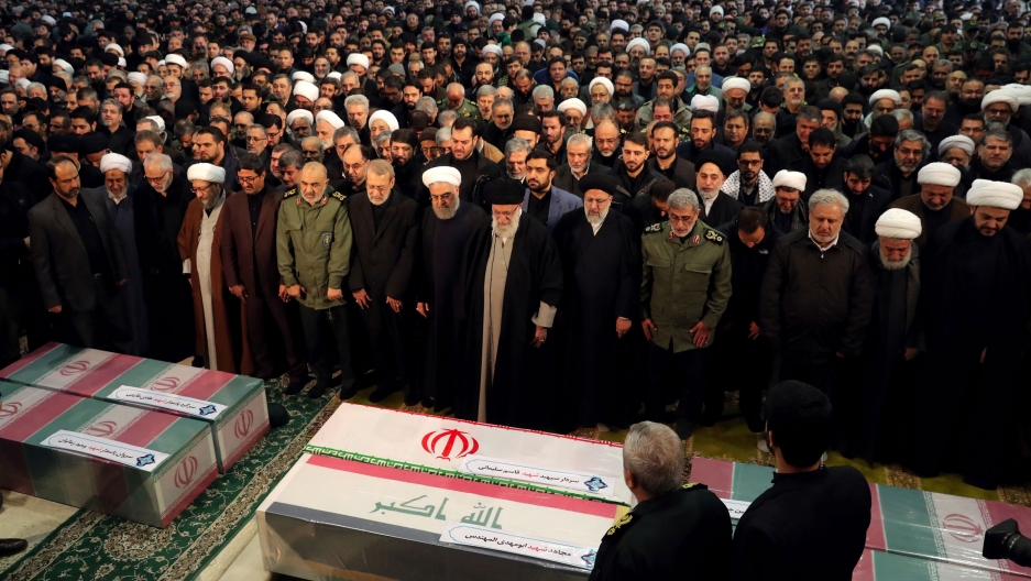 Iran's Supreme Leader Ayatollah Ali Khamenei and President Hassan Rouhani pray near the coffins of Iranian Maj. Gen. Qasem Soleimani, head of the elite Quds Force, and Iraqi militia commander Abu Mahdi al-Muhandis. Iran's Supreme Leader Ayatollah Ali Khamenei and President Hassan Rouhani are shown in front of a large group of people with their heads bowed and praying.