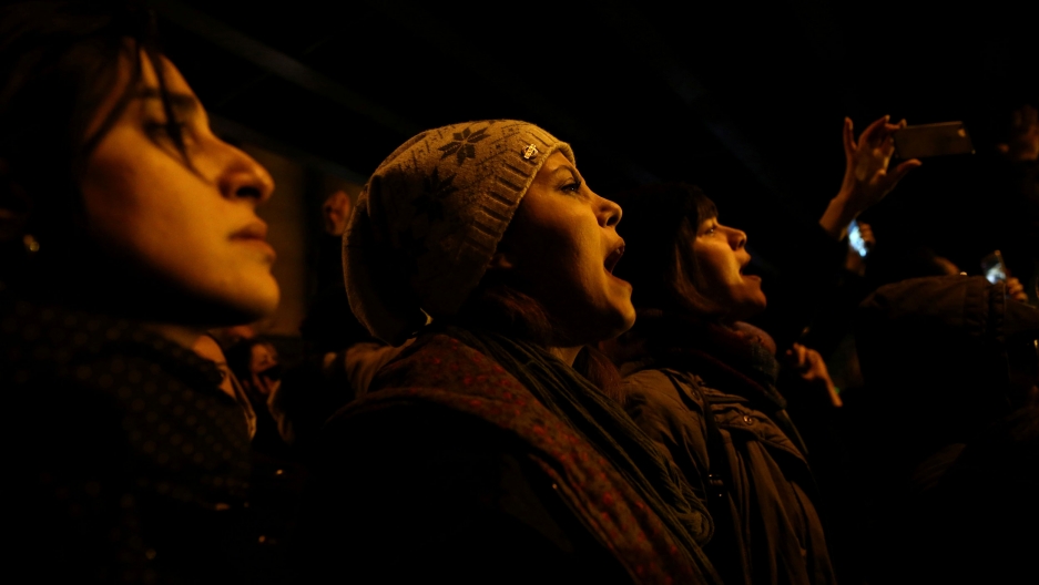 A woman shouts slogans as she gathers with people to show their sympathy to the victims of the crash of Ukrainian AIrlines flight PS752, in Tehran, Iran, Jan 11, 2020. Several people are shown with their mouths agape and shouting in the dark of the night.