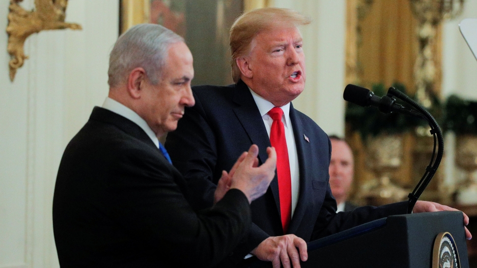 US President Donald Trump and Israel's Prime Minister Benjamin Netanyahu hold a joint news conference to discuss a new Middle East peace plan at the White House in Washington, DC, Jan. 28, 2020. US President Donald Trump is shown speaking from a podium with Israel's Prime Minister Benjamin Netanyahu shown standing next to him clapping.