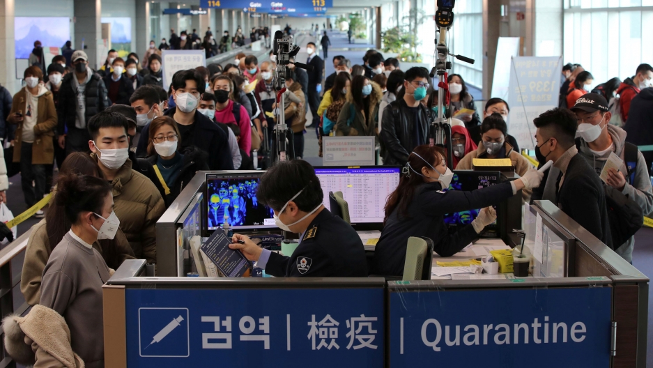 Passengers from China get a fever check upon their arrival at Incheon International Airport in Incheon, South Korea, Jan. 29, 2020. A crowd of people are shown in an airport wearing facemasks and waiting in lines.