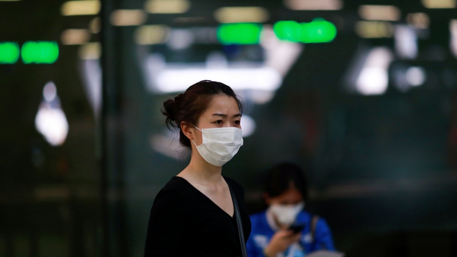 A tourist wears a mask to prevent the spread of the new coronavirus as she arrives at the Suvarnabhumi Airport in Bangkok, Thailand, Feb. 3, 2020. A woman is shown wearing a dark shirt and a white face mask over her nose and mouth.