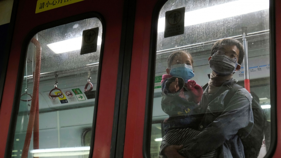 Passengers wear face masks in a Hong Kong bound train at Lo Wu MTR station, before the closing of the Lo Wu border following the coronavirus outbreak in Hong Kong, Feb. 3, 2020. A man is shown holding a child, both wearing face masks, and shown through the window of a train.