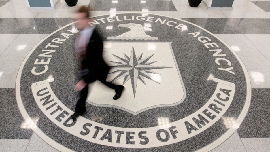The lobby of the CIA Headquarters Building in McLean, Virginia. A seal of the CIA is shown from above with a person walking over it in blurred focus.