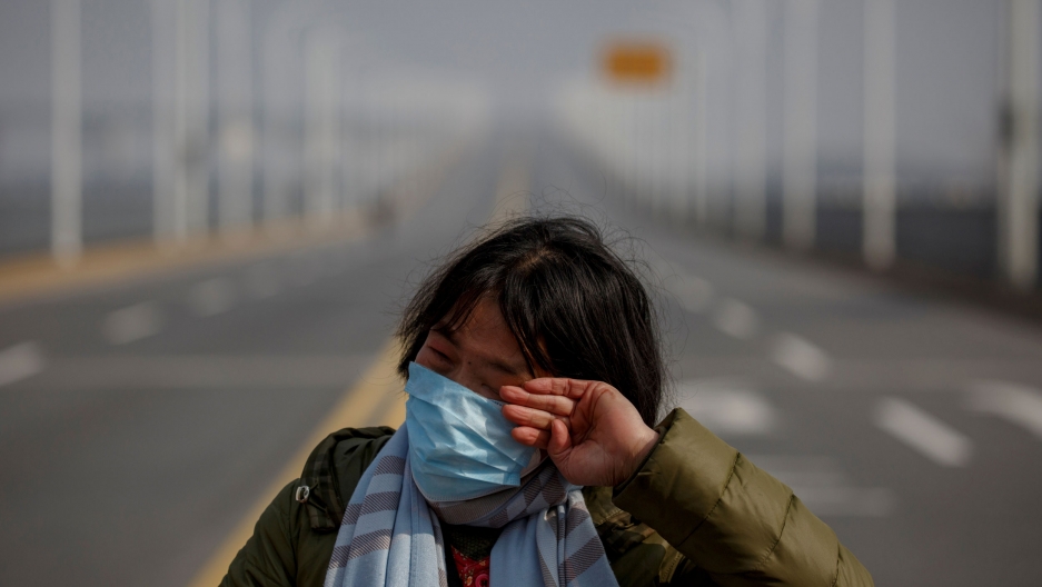 A mother reacts as she pleads with police to allow her daughter to pass a checkpoint after she arrived from Hubei province in Jiujiang, China, Feb. 1, 2020. A woman is shown wearing a face mask and stripped scarf while standing on the edge of an empty bridge.