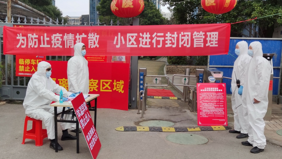 Workers in protective suits are seen at a checkpoint for registration and body temperature measurement, at an entrance to a residential compound in Wuhan, China Feb. 13, 2020. Several workers are shown wearing full medical protective suits and face masks.