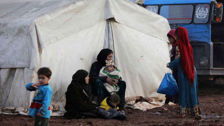 Internally displaced people sit outside tents at a makeshift camp in Azaz, Syria, Feb. 19, 2020. Two women wearing black hijabs are shown with several children in front of a white tent.