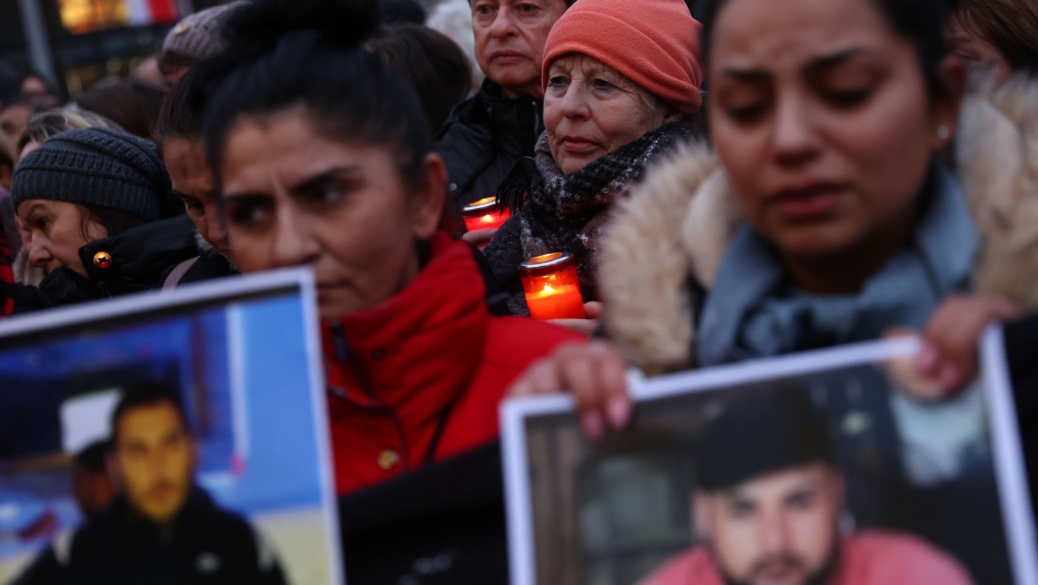 People attend a vigil for the victims of a shooting in Hanau, near Frankfurt, Germany, Feb. 20, 2020. A large group of people are shown at a vigil with several holding candles and photographs.